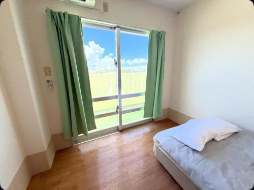 a bedroom with a bed and a large window at ハイ沖縄金武店トイレお風呂共用 プレオープン中駐車場有 ペット同伴可能長期滞在可能2025年10月より車貸し出しサービス有希望であればお申し付けください in Kin