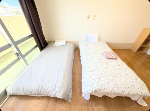 two beds in a room with a large window at ハイ沖縄金武店トイレお風呂共用 プレオープン中駐車場有 ペット同伴可能長期滞在可能2025年10月より車貸し出しサービス有希望であればお申し付けください in Kin