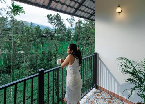una donna in abito bianco che tiene una tazza su un balcone di The Feel Munnar Resort & Spa a Munnar