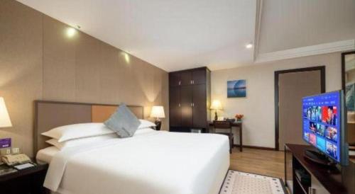 a bedroom with a large white bed and a television at Zhuhai Aqueen Hotel in Zhuhai