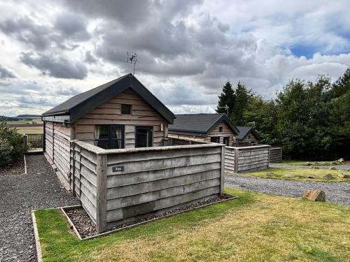 a wooden house with a fence in front of it at Fox Lodge with Hot Tub in Cupar