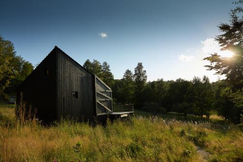 a black building in a field with the sun in the sky at BIOSFERA Natural Experience Domki Premium w Karkonoszach in Przesieka