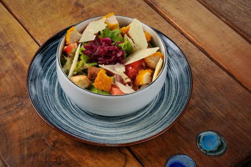 a bowl of salad on a plate on a wooden table at Auberge de la fontaine aux loups in Saint-Sulpice-le-Dunois