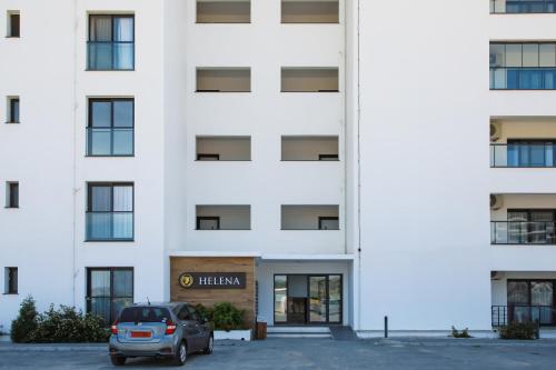 un coche aparcado delante de un edificio blanco en Helena Sea Breeze Apartments - Resort Living with Pools & Full Facilities, en Rizokarpaso