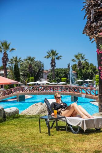 a man and woman sitting in a lawn chair next to a pool at Palmin Hotel in Kusadası