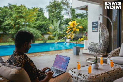 a man sitting on a couch with a laptop at StayVista at The Amaryllis with Heated Pool & Projector Set-Up in Karjat