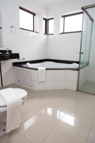 a white bathroom with a tub and a toilet at Hotel Ouro Lavras in Lavras