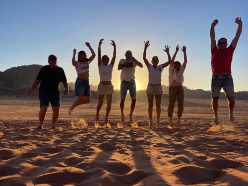 a group of people jumping on the beach at Wadi Rum Star Camp in Wadi Rum