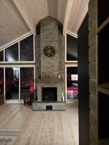 a living room with a stone fireplace and windows at Skogshytte på Skreia in Brattlia