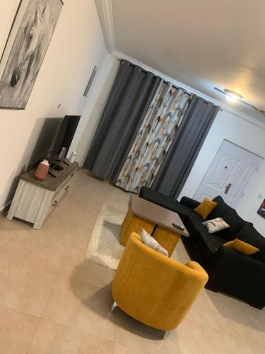 a living room with a black couch and yellow chairs at Cozy comfortable One bedroom close to Airport in Accra