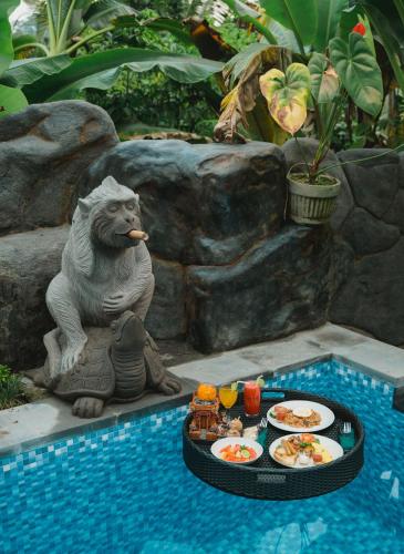Eine Statue sitzt neben einem Pool mit Tellern voller Essen in der Unterkunft Villa Gong Sebatu in Ubud