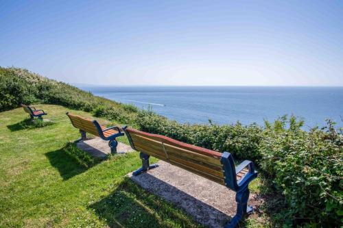 three park benches sitting on a hill overlooking the ocean at Langcliffe Park - 2 Bedroom Chalet - Mumbles in Swansea