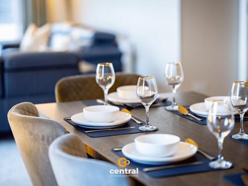 a wooden table with wine glasses and plates on it at CENTRAL SERVICED APARTMENTS - City Quay - 2 Bedrooms - En-Suite Bathroom - Dedicated Parking Space - Fully Equipped - Walk Away From Dundee Bus & Train Station - Close to City Centre with River Views and Balcony - NEW in Dundee