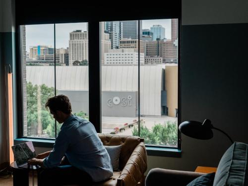a man sitting on a couch reading a book in front of a window at The Junto Hotel in Columbus