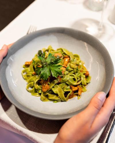 a person holding a plate of pasta with greens at Hotel Oberwirt in Verano