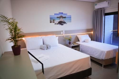 una camera d'albergo con due letti e una pianta in vaso di Hotel & Pousada Porto Ubá a Lidianópolis