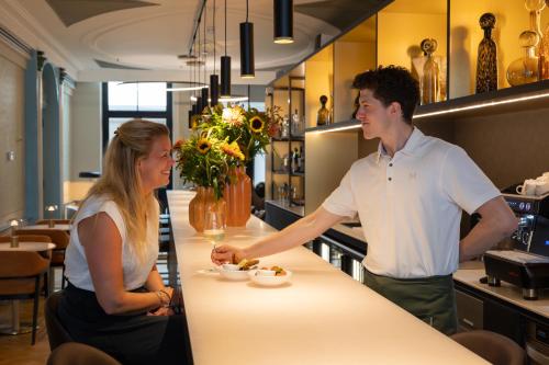 a man and a woman standing at a counter in a restaurant at Hotel Maison Maastricht Centrum - Handwritten Collection in Maastricht