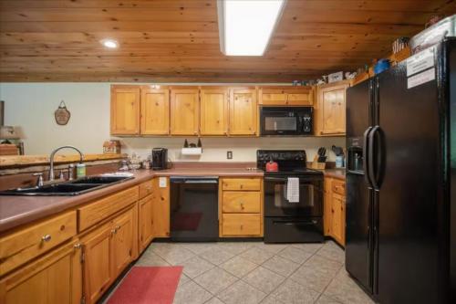 a kitchen with wooden cabinets and a black refrigerator at Cowboy Cabin - Creekside Firepit, Pool Table, Games + Large Screened-In Porch in Aska