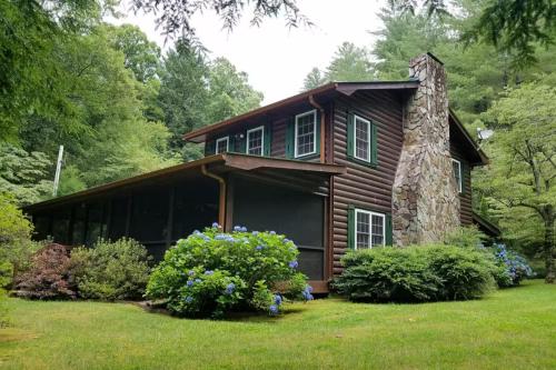 a log cabin with flowers in front of it at Cowboy Cabin - Creekside Firepit, Pool Table, Games + Large Screened-In Porch in Aska