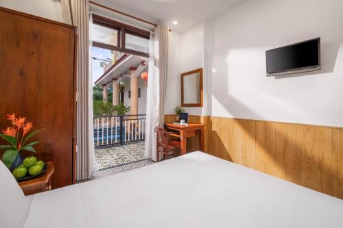a bedroom with a bed with a television and a balcony at Sala Hoi An Hotel in Hoi An
