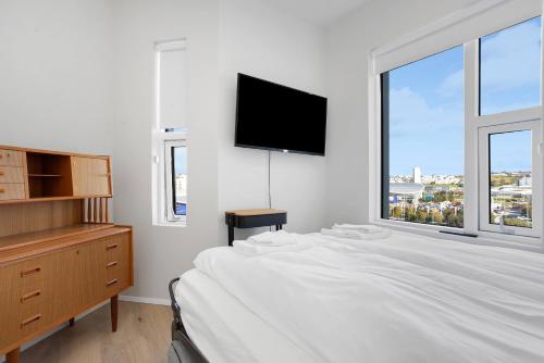 a white bedroom with a bed and a tv on the wall at Spacious 2BR Apt with Balcony, Sauna and Free Parking in Reykjavík