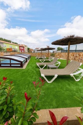 a group of lounge chairs and umbrellas on a lawn at Casa El Rincón de Alberto con Piscina CLIMATIZADA y Calefacción in Camelle
