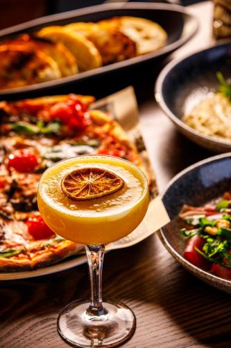 a glass of orange juice sitting on a table with pizzas at ibis London Canning Town in London