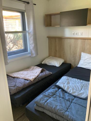 two beds in a small room with a window at Mobil Home 6 personnes in Biscarrosse