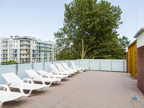 a row of white lounge chairs on a balcony at 3L Apartments Bliżej Morza in Kołobrzeg