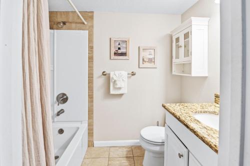 a white bathroom with a sink and a toilet at Walk to Beach, Pool & Flagler! Relaxed Condo with Balcony & Full Kitchen in Chicken Island
