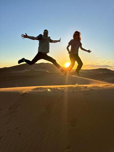 two people jumping in the sand in the desert at Aladdin merzouga camp in Merzouga