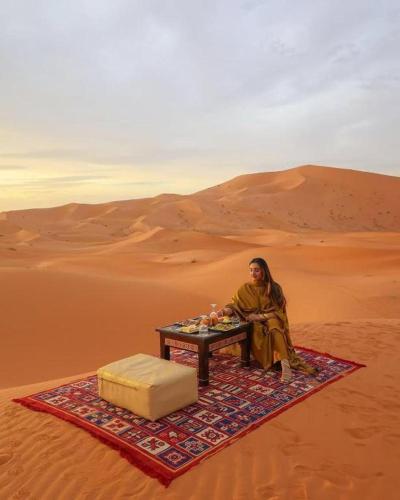 a woman sitting on a table in the desert at Aladdin merzouga camp in Merzouga