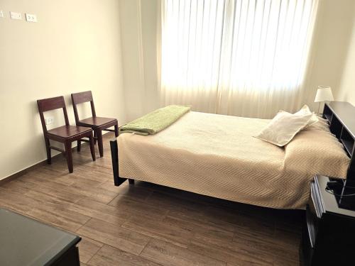 a bedroom with a bed and two chairs and a window at Departamento Céntrico en Primer Piso in Tacna