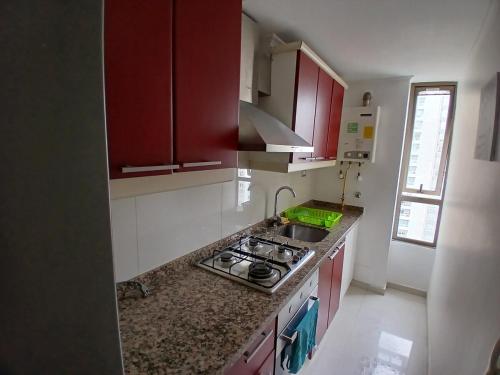 La cuisine est équipée de placards rouges et d'un four avec plaques de cuisson. dans l'établissement departamento cómodo y central, à Santiago