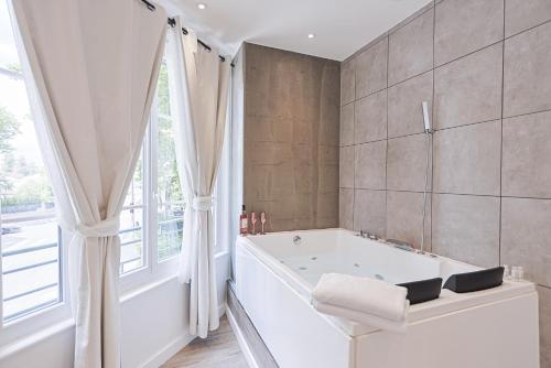 a white bathroom with a tub and a window at LES BULLES DE MONA - Chic - Spa - Clim in Lyon