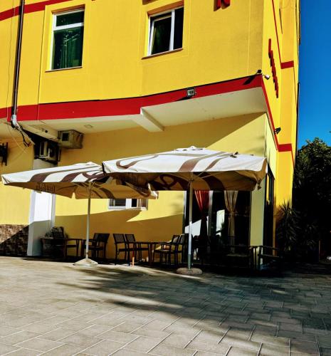 two umbrellas and tables in front of a building at London Restaurant Hotel in Kukës