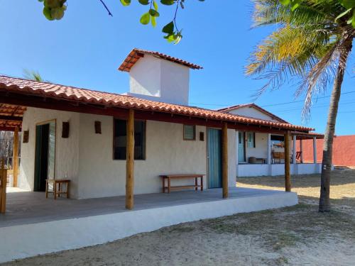 a white building with a porch and a palm tree at Céu - Quarto com entrada privada in Luis Correia