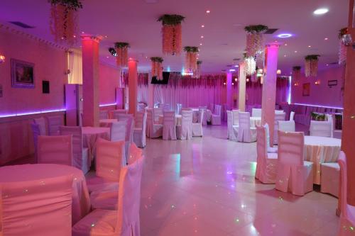 a room with white chairs and tables and pink lighting at London Restaurant Hotel in Kukës