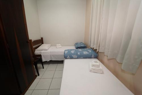 a room with two beds and a chair and curtains at Eventos & Hospedagem Sagrada Família in Sao Paulo