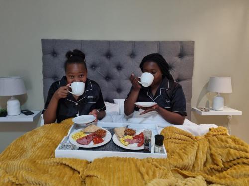 two women sitting in bed drinking coffee and eating food at La Exotica Lodge & Spa in Rustenburg
