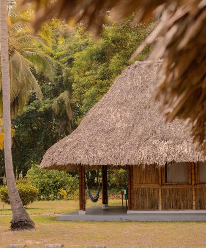 a hut with a thatched roof and a palm tree at Hotel Playa Bonita Tayrona in Buritaca
