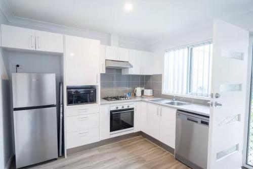 a kitchen with white cabinets and a stainless steel refrigerator at Green Olive in Ettalong Beach