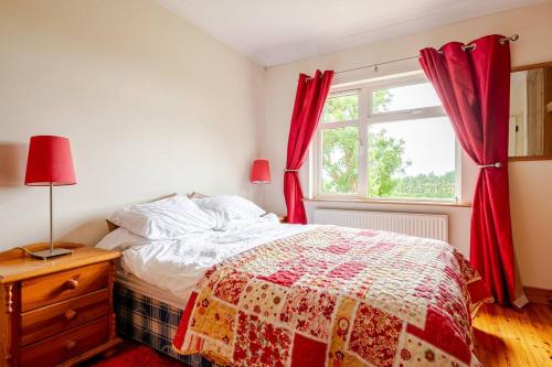 a bedroom with a bed with red curtains and a window at Spacious Home by Lough Rynn Castle Wedding Venue in Mohill
