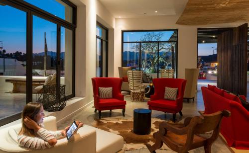 a woman sitting on a couch in a living room with red chairs at Hotel El Ganzo - Adults Only in San José del Cabo