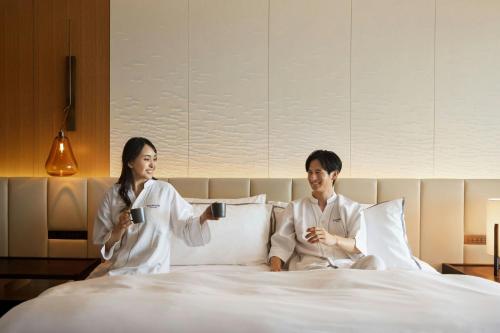a man and woman sitting on a bed holding coffee cups at The Westin Yokohama in Yokohama