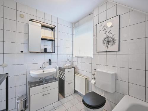 a white tiled bathroom with a toilet and a sink at Aan de oever in Stevensweert