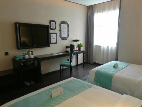 a hotel room with two beds and a desk with a television at Xana Hotelle·Tianshui Shangyi Plaza in Tianshui