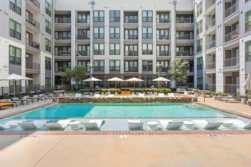 an apartment pool with chairs and umbrellas in front of a building at Stylish 1BR Retreat in Houstons Sawyer Yard Art District Minutes to Downtown in Houston