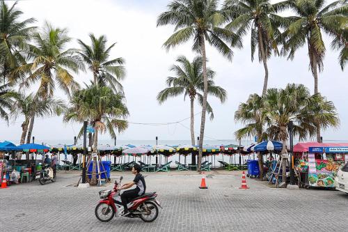 a man riding a motorcycle on a beach with palm trees at Sea View and Hill View Room for 6 Guests, Bangsaen Royal Beach by Cozy Corner in Ban Laem Thaen
