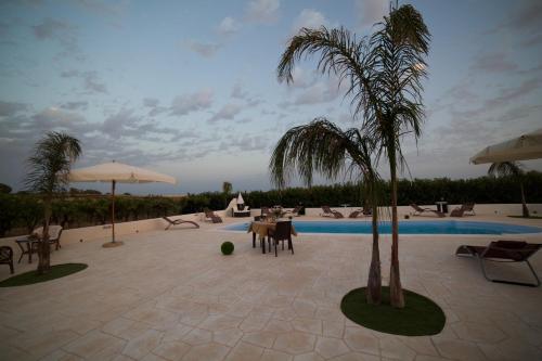 a patio with a pool and palm trees and chairs at Le Zarafe in Caltabellotta